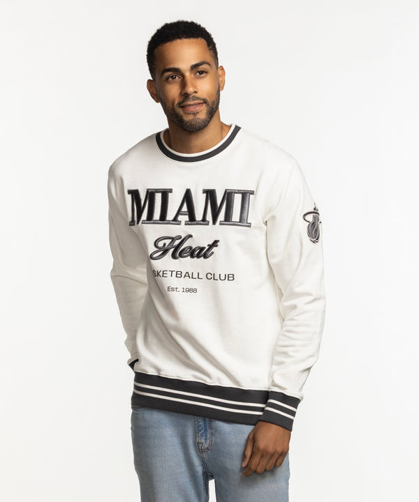 A man wears the Sportiqe Miami HEAT Basketball Club Crewneck, featuring black trim and lettering, styled over light blue jeans against a white background. This crewneck by Sportiqe offers a standard fit for comfort and versatile wear.