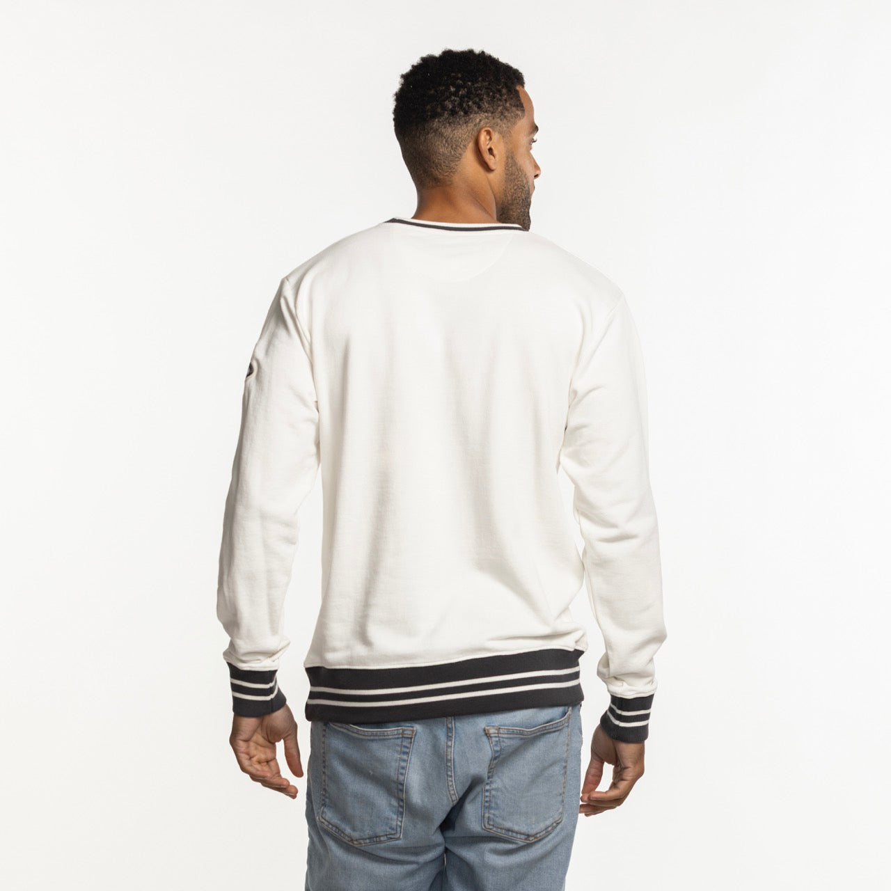 A man faces away from the camera, wearing a Sportiqe Miami HEAT Basketball Club Crewneck by Sportiqe—white with black striped cuffs and waistband—paired with light blue jeans, set against a plain white background.