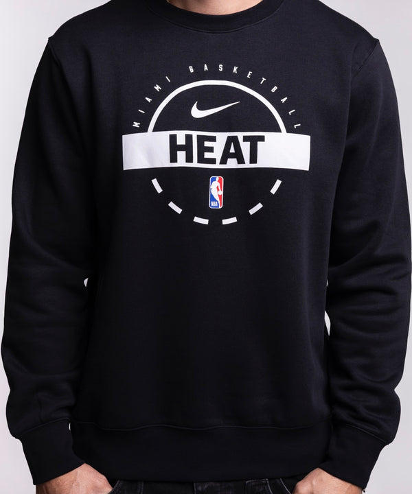 A man smiles and looks left while wearing the Nike Miami HEAT 2025-26 On-Court Practice Crewneck, featuring the Nike logo and HEAT text on the front, standing against a plain light background.