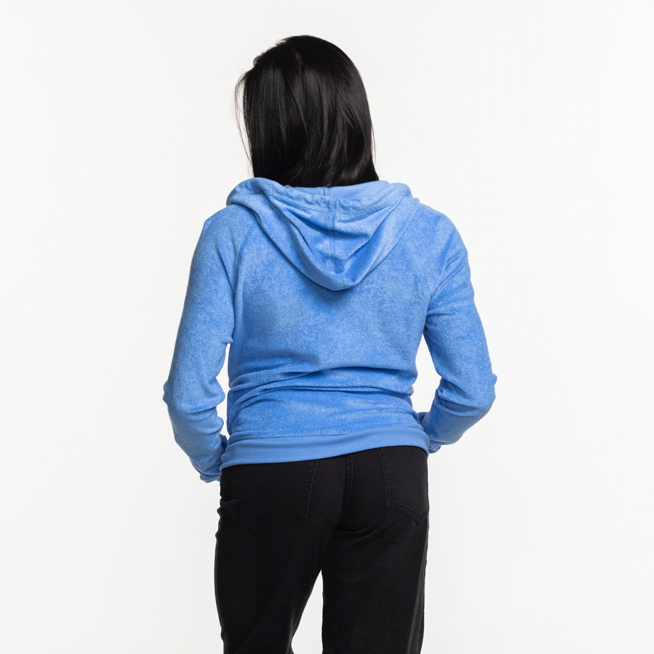 A woman with long dark hair, seen from behind, wears the Antigua Miami HEAT Original Vice Nights Women's Zip Up Jacket by Antigua and black pants, standing against a plain white background.