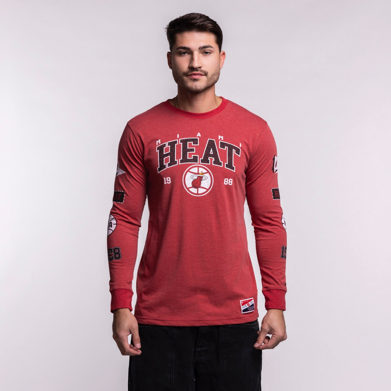 A man stands facing forward wearing the New Era Miami HEAT Red Cuffed Long Sleeve Tee, featuring a HEAT basketball logo and 