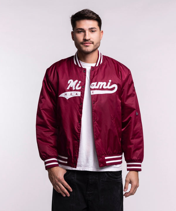 A man faces forward wearing a Hype and Vice Miami HEAT Varsity Jacket in maroon with white script, paired with a white t-shirt and black pants, set against a plain light background.