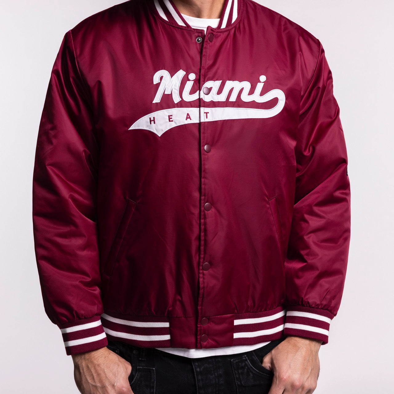 A person wearing a Hype and Vice Miami HEAT Varsity Jacket, maroon with white striped cuffs and collar, plus 