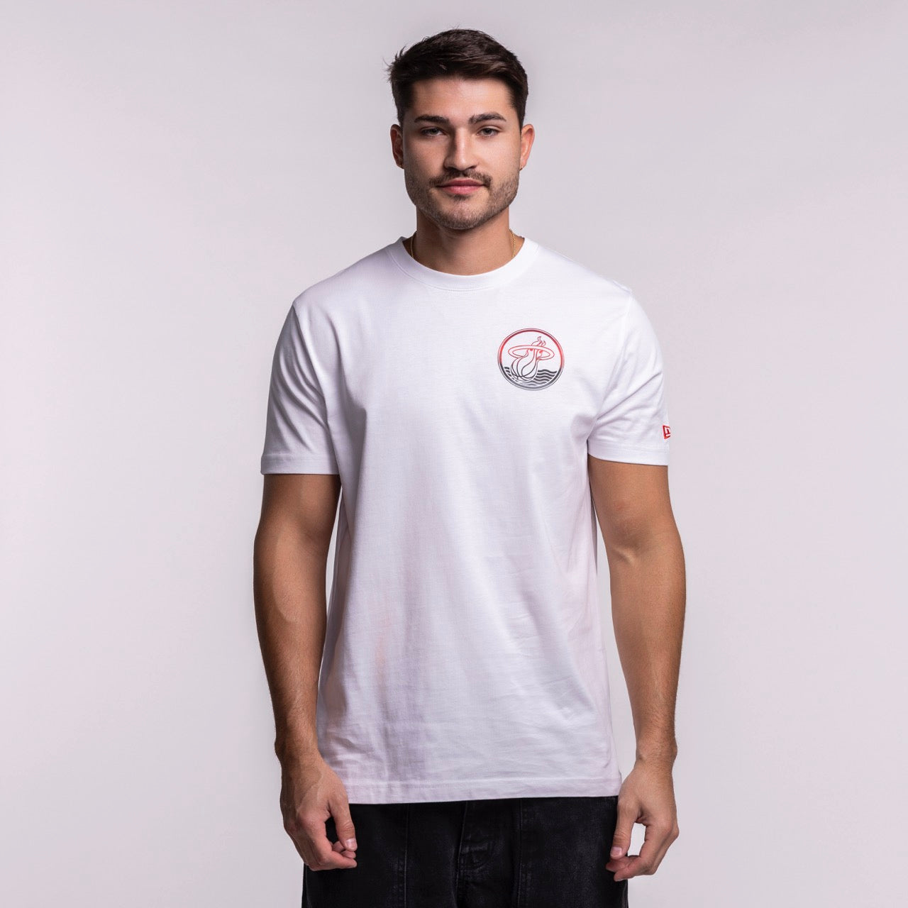 A man with short dark hair and a trimmed beard wears the New Era Miami HEAT White Basketball Tee, a standard fit 100% cotton T-shirt with a small red and gray graphic on the left chest, standing against a light gray background.