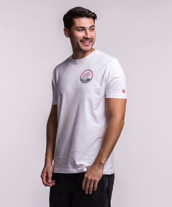 A man with short dark hair and a beard stands sideways, smiling in a New Era Miami HEAT White Basketball Tee and black pants, against a plain light background.