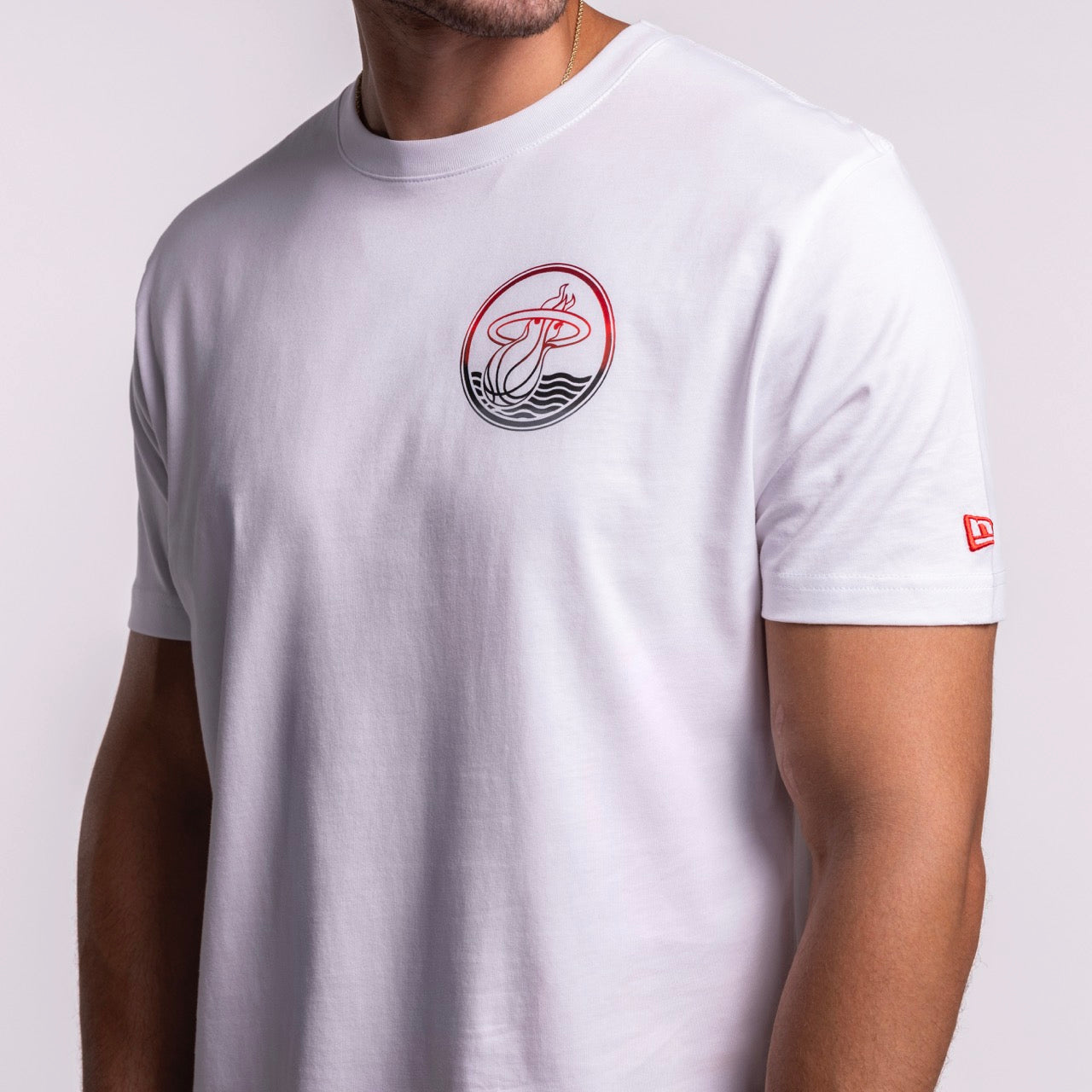 A person wears the New Era Miami HEAT White Basketball Tee—100% cotton, standard fit, with a round red and black stylized waves and 