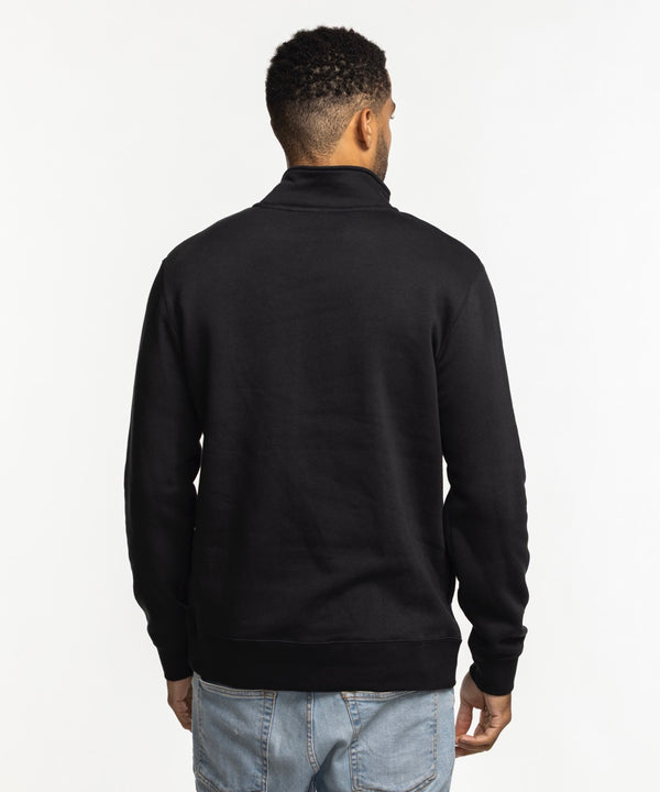 A man smiles against a white background wearing the Nike Miami HEAT Original Vice Nights 1/2 Zip Fleece Jacket—standard fit, made from a cotton-poly blend, featuring “Miami” on the chest—paired with light blue jeans.