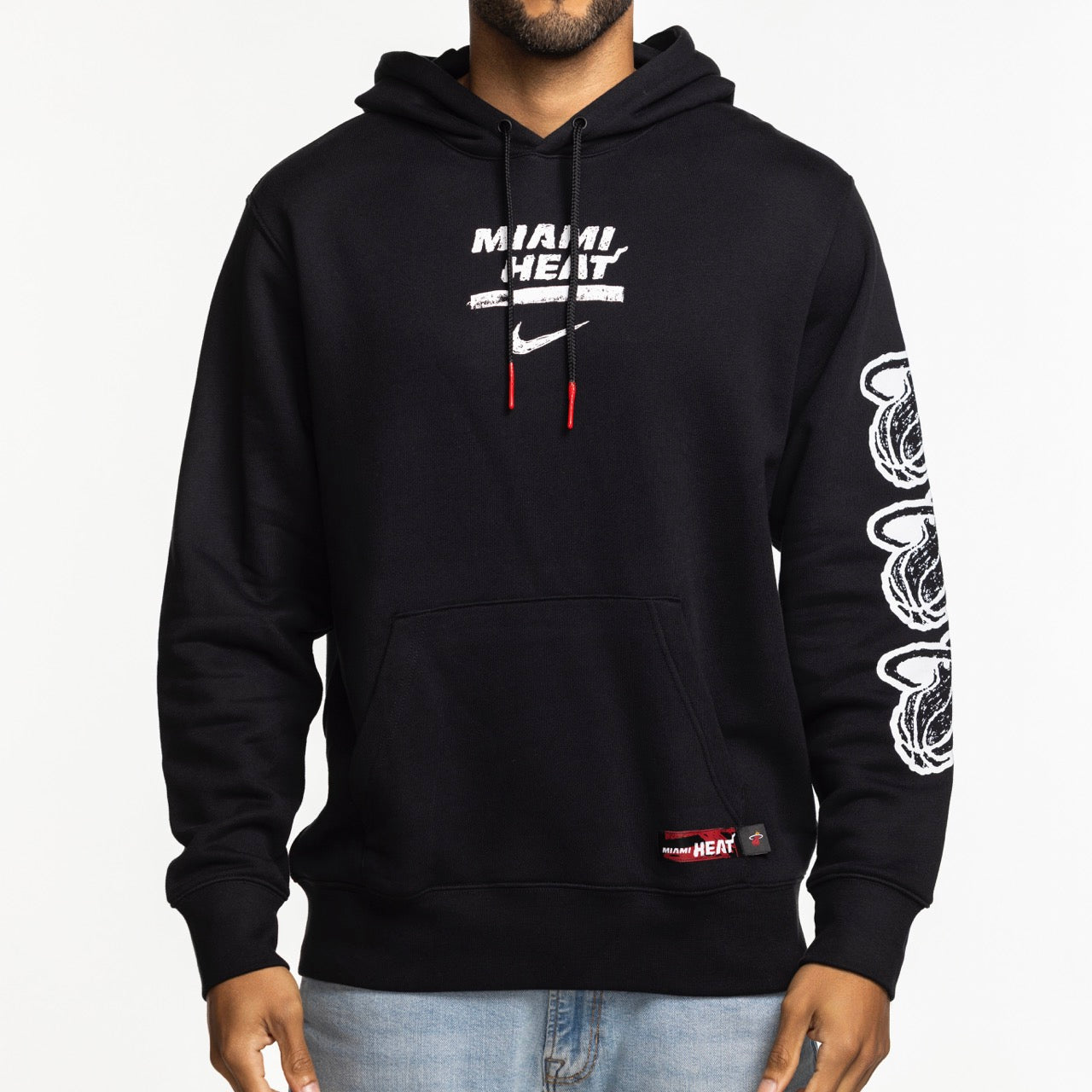 A person wears the Nike Miami HEAT Club Pullover Black Hoodie featuring the team logo and Nike swoosh on the chest, standard fit, white flaming basketballs down the right sleeve, a front pocket, red-tipped drawstrings, and 100% cotton build.