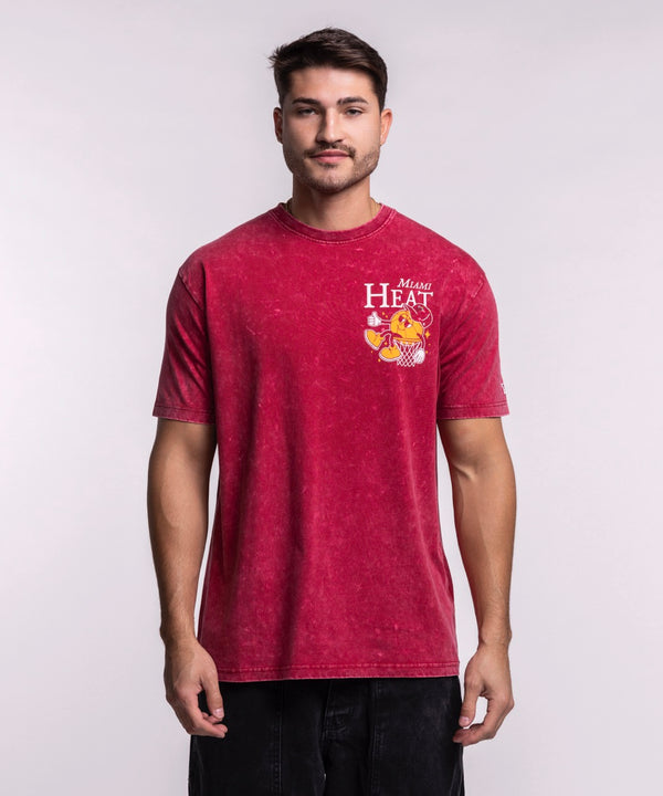A man wears the New Era Miami HEAT Ball Character Tee, featuring a cartoon mascot graphic on red. This standard fit t-shirt by New Era is made of 100% cotton and is machine washable for easy care, shown against a plain light background.