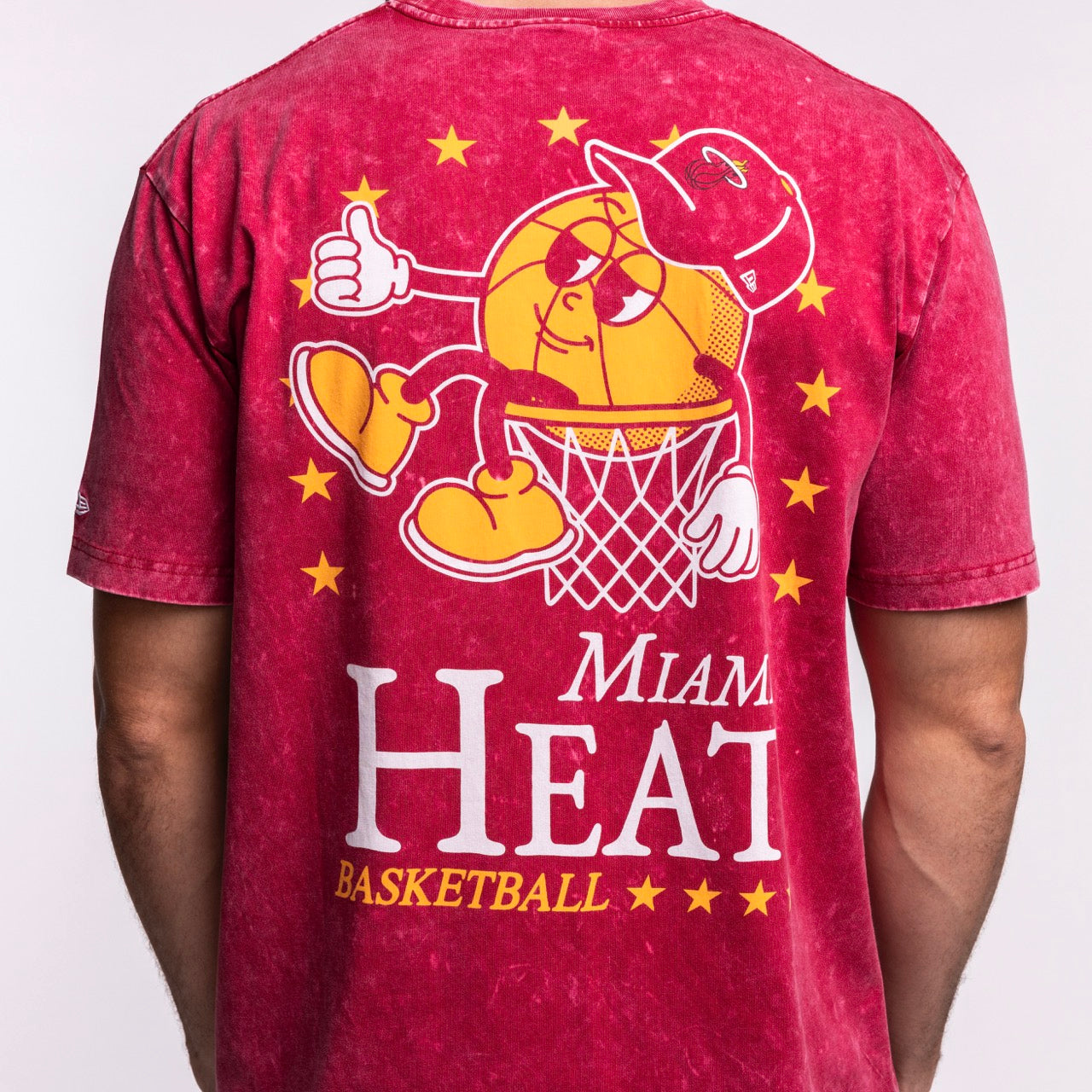 Wearing the New Era Miami HEAT Ball Character Tee, a 100% cotton red shirt by New Era, featuring a cartoon basketball with sunglasses, sneakers, and a thumbs-up in a hoop surrounded by stars.