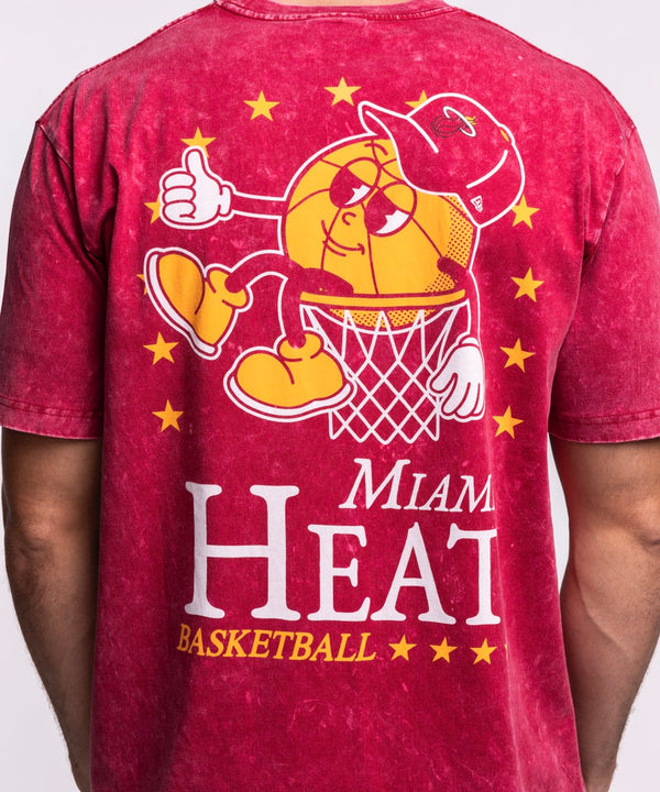 A man wears the New Era Miami HEAT Ball Character Tee, featuring a cartoon mascot graphic on red. This standard fit t-shirt by New Era is made of 100% cotton and is machine washable for easy care, shown against a plain light background.