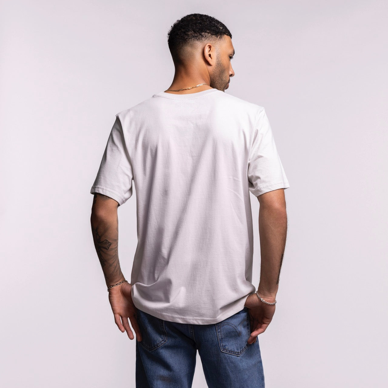 A man faces away from the camera, wearing the Sportiqe Miami HEAT 1988 Basketball Tee by Sportiqe and blue jeans. The 100% cotton shirt is set against a light studio background. Machine wash cold recommended.