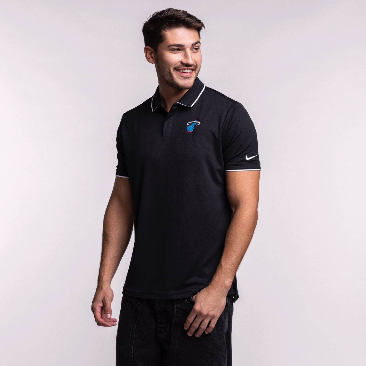 A man wearing a size L Nike Miami HEAT Original Vice Nights Logo Polo, with the Miami Heat logo and Nike swoosh on the sleeve, smiles and looks left against a plain light background.