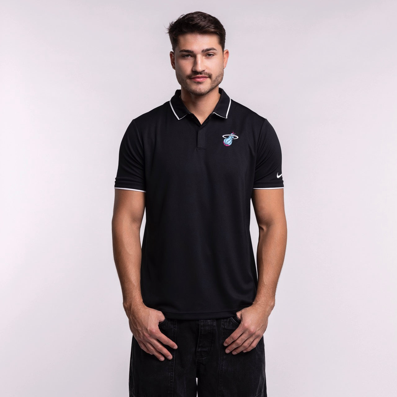 A man with short brown hair and a mustache wears a Size L Nike Miami HEAT Original Vice Nights Logo Polo in black with white trim, standing against a plain light background with his hands at his sides.