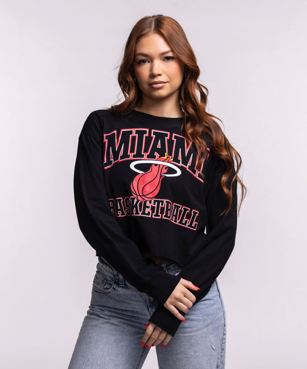A young woman with long wavy hair stands against a plain light background wearing a black Court Culture 