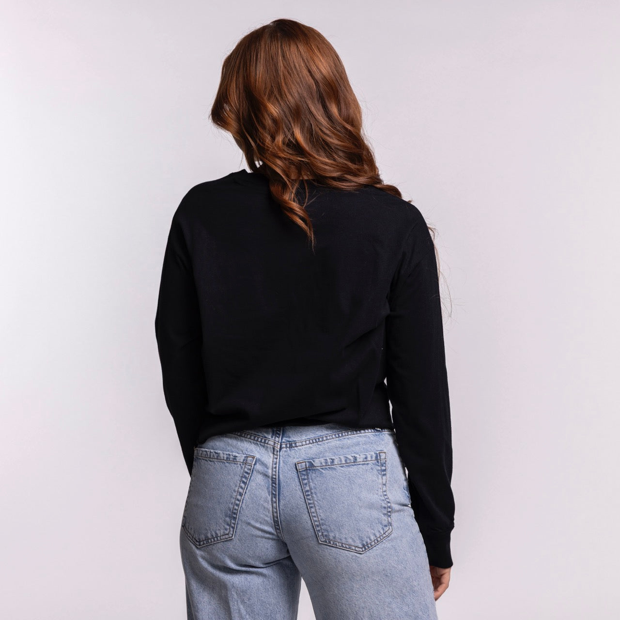 A person with long, wavy brown hair stands with their back to the camera, wearing the Court Culture 