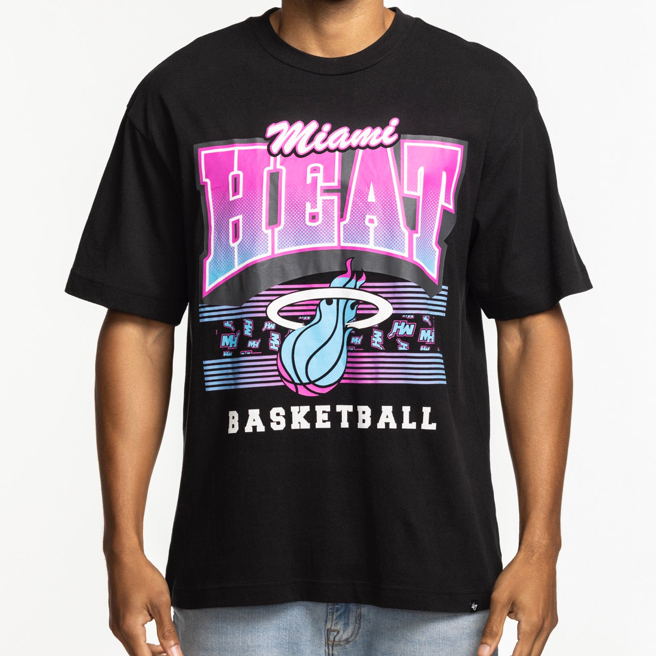 Someone models the '47 Brand Miami HEAT Original Vice Nights Foundation Tee, a black cotton shirt with bold pink, white, and blue graphics plus the team logo on the front. The standard fit tee is machine washable. The person’s head is not visible against a white background.