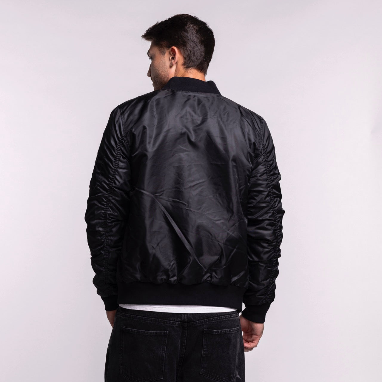 A man faces away from the camera, wearing a G-III Sports Miami HEAT Original Vice Nights Aviator Jacket and black jeans against a plain light background.