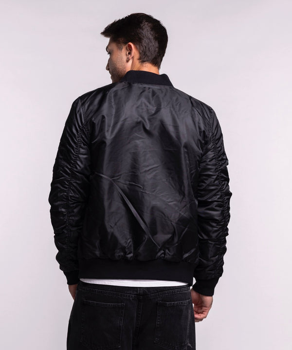 A man models the G-III Sports Miami HEAT Original Vice Nights Aviator Jacket in men's size L, standing against a plain light background and looking at the camera while holding the polyester, standard fit jacket front. Machine wash cold.