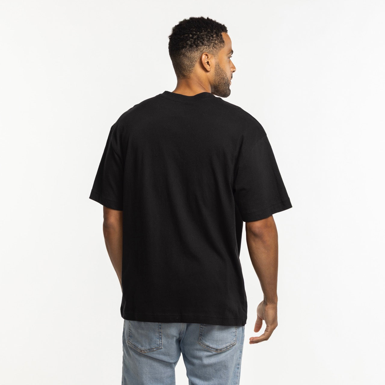 A man stands with his back to the camera, wearing a '47 Brand Miami HEAT Original Vice Nights Foundation Tee and light blue jeans against a white background.