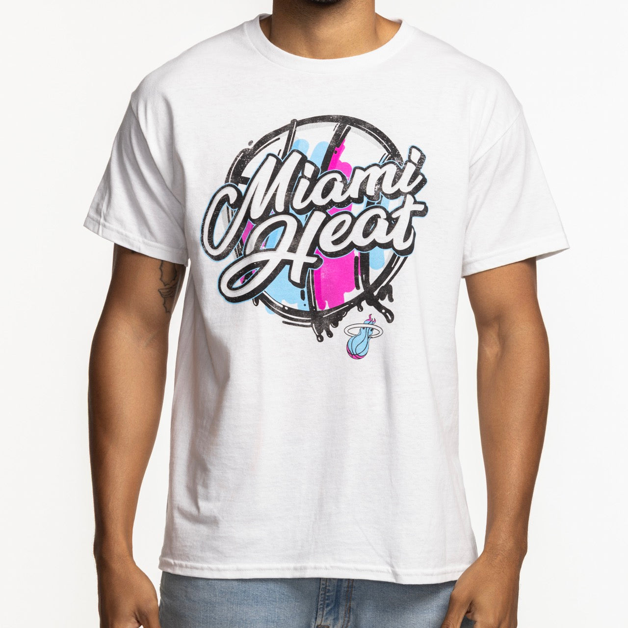 A person wears the Miami HEAT Original Vice Nights White Tee by Item Of The Game, a standard-fit cotton shirt with bold Miami Heat script in blue and pink accents and a small Heat basketball logo below. Machine washable for easy care.