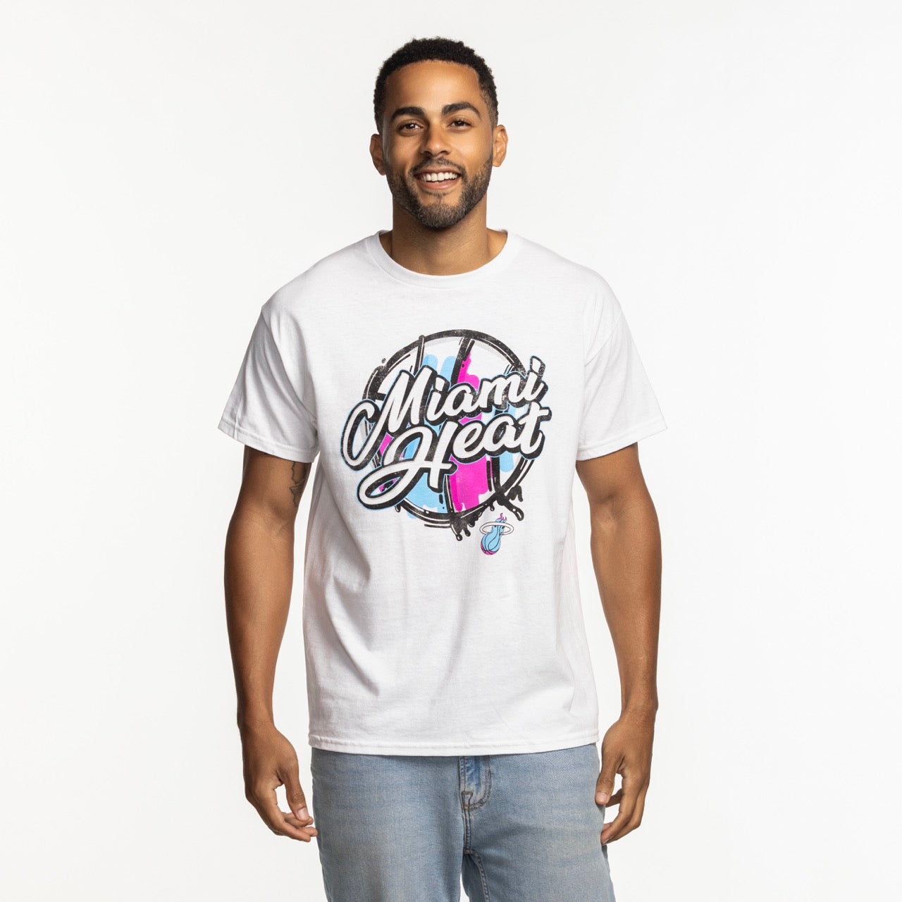 A man smiles against a white background, wearing the Item Of The Game Miami HEAT Original Vice Nights White Tee and light blue jeans.
