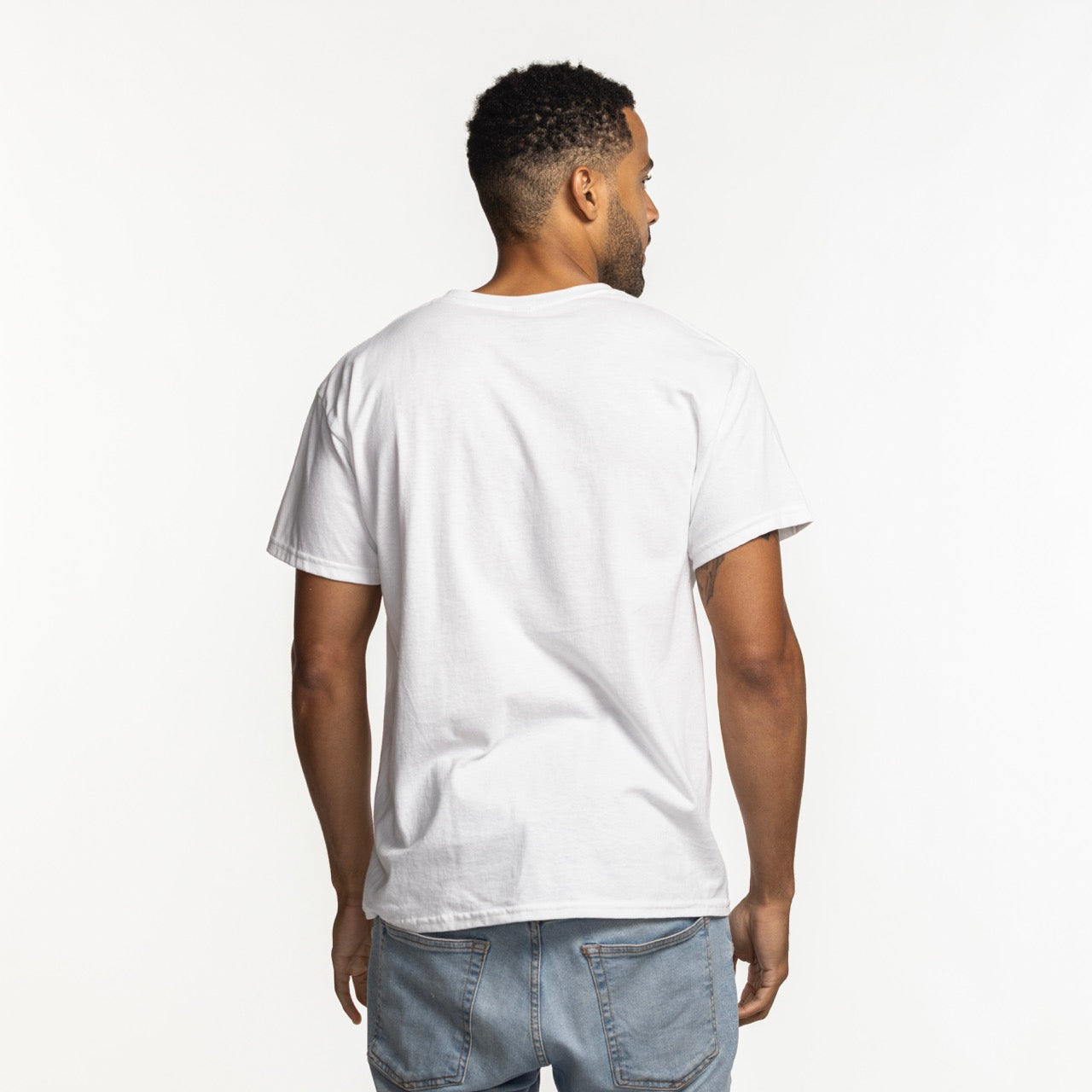A man faces away from the camera wearing the Miami HEAT Original Vice Nights White Tee by Item Of The Game, a soft, comfortable, machine-washable cotton t-shirt in a standard fit with light blue jeans against a white background.