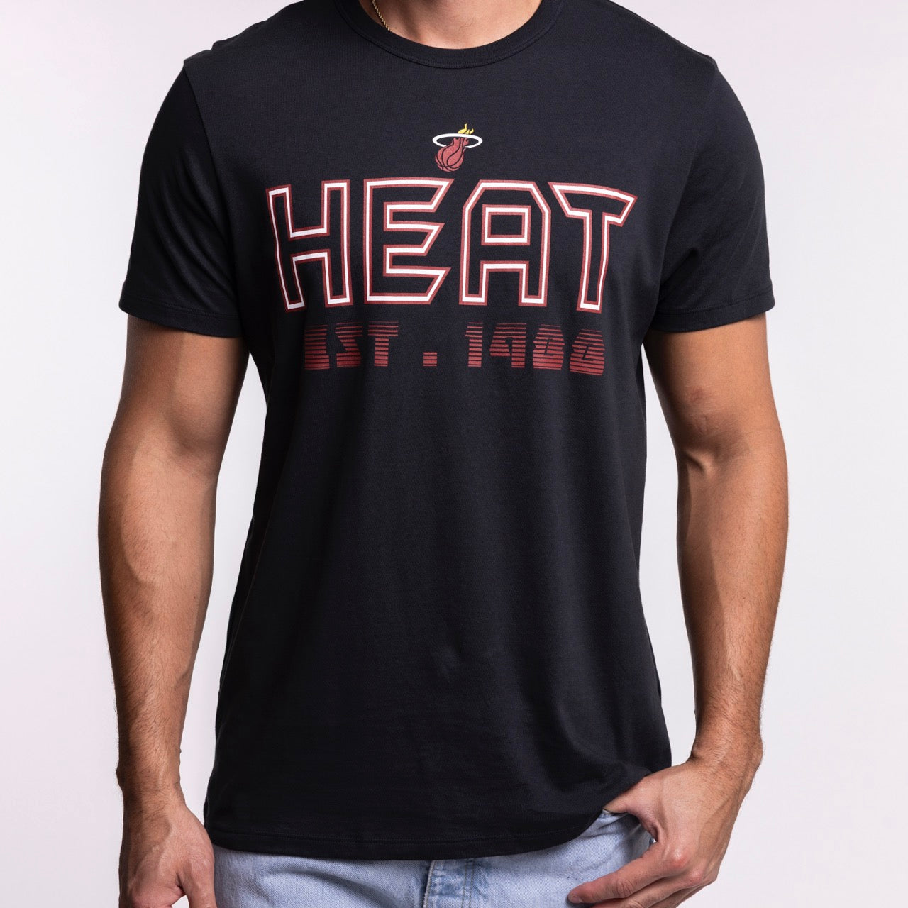 A person wears the '47 Brand Miami HEAT Byline Franklin Tee, a black 100% cotton T-shirt featuring the Miami Heat logo and bold red 