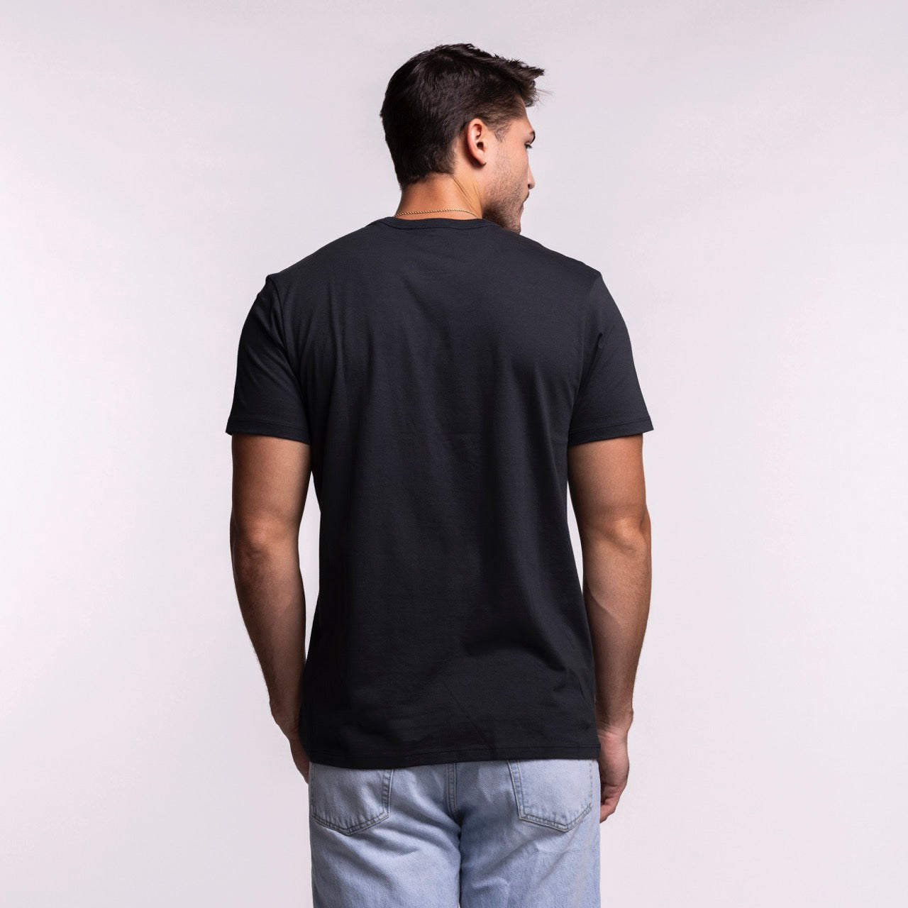 A man stands facing away from the camera, wearing a '47 Brand Miami HEAT Byline Franklin Tee and light blue jeans against a light background.