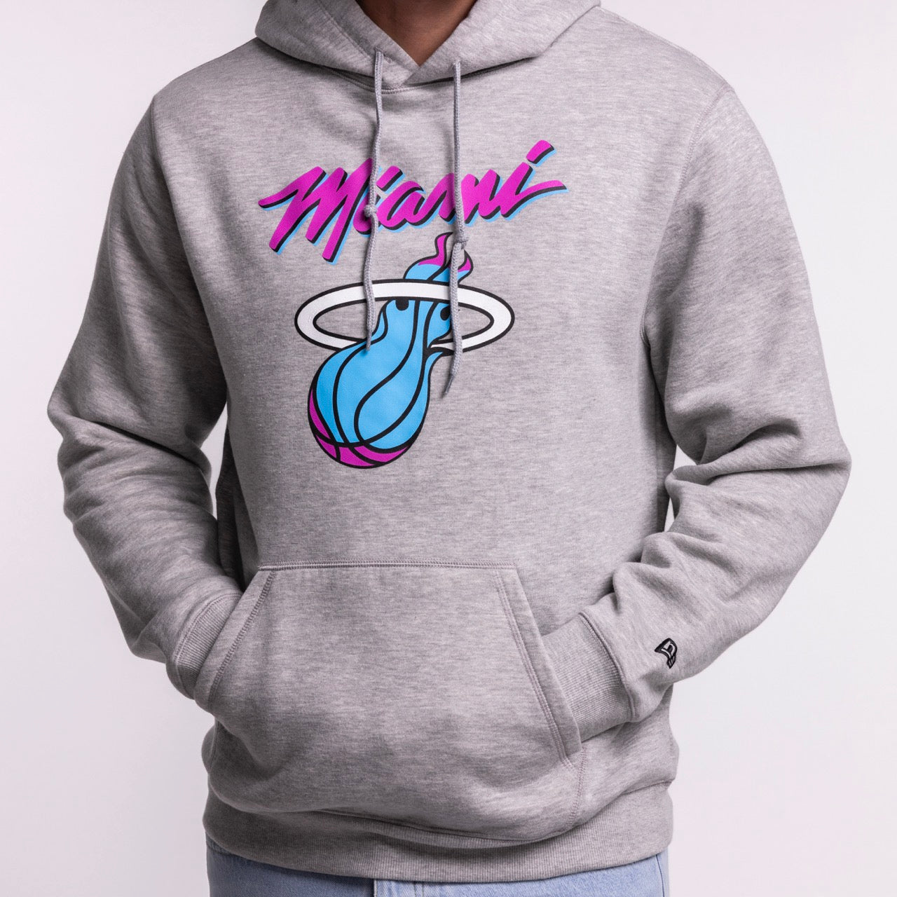 Someone wears the New Era Miami HEAT Original Vice Grey Hoodie—a light gray, standard fit hoodie with pink and blue 