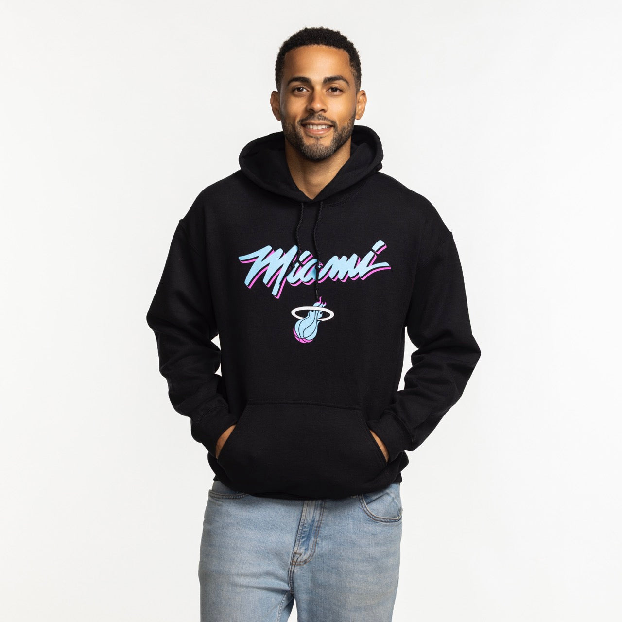 A man in a standard fit black Miami HEAT Original Vice Nights Logo Hoodie by Item Of The Game, featuring colorful Miami and basketball graphics on soft cotton-polyester, stands smiling with hands in pockets against a white background.
