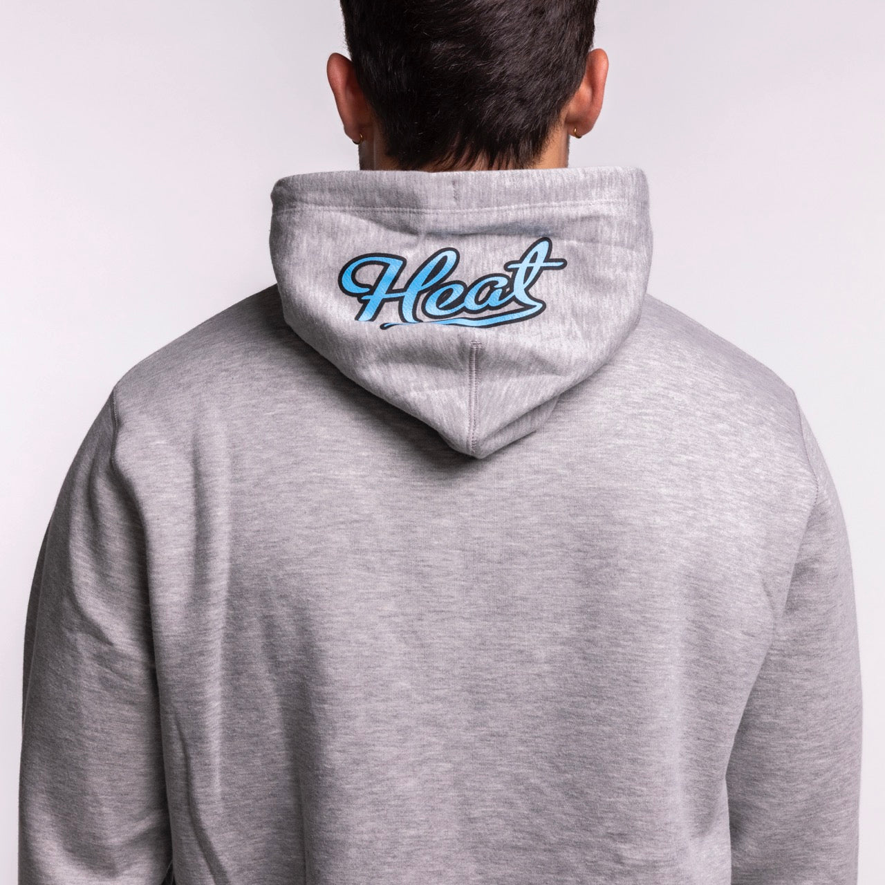 A person seen from behind wears the New Era Miami HEAT Original Vice Grey Hoodie, a light gray standard fit made from a cotton-polyester blend, featuring 