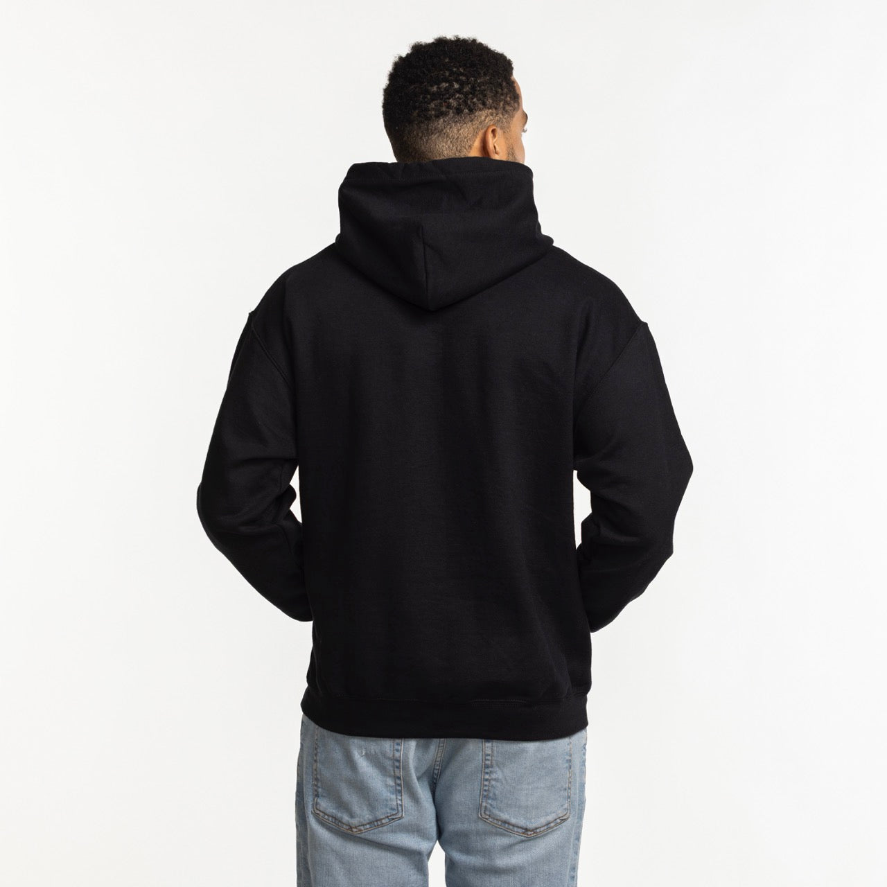 A person stands facing away from the camera, wearing the Item Of The Game Miami HEAT Original Vice Nights Logo Hoodie in black with the hood down and light blue jeans, against a plain white background.