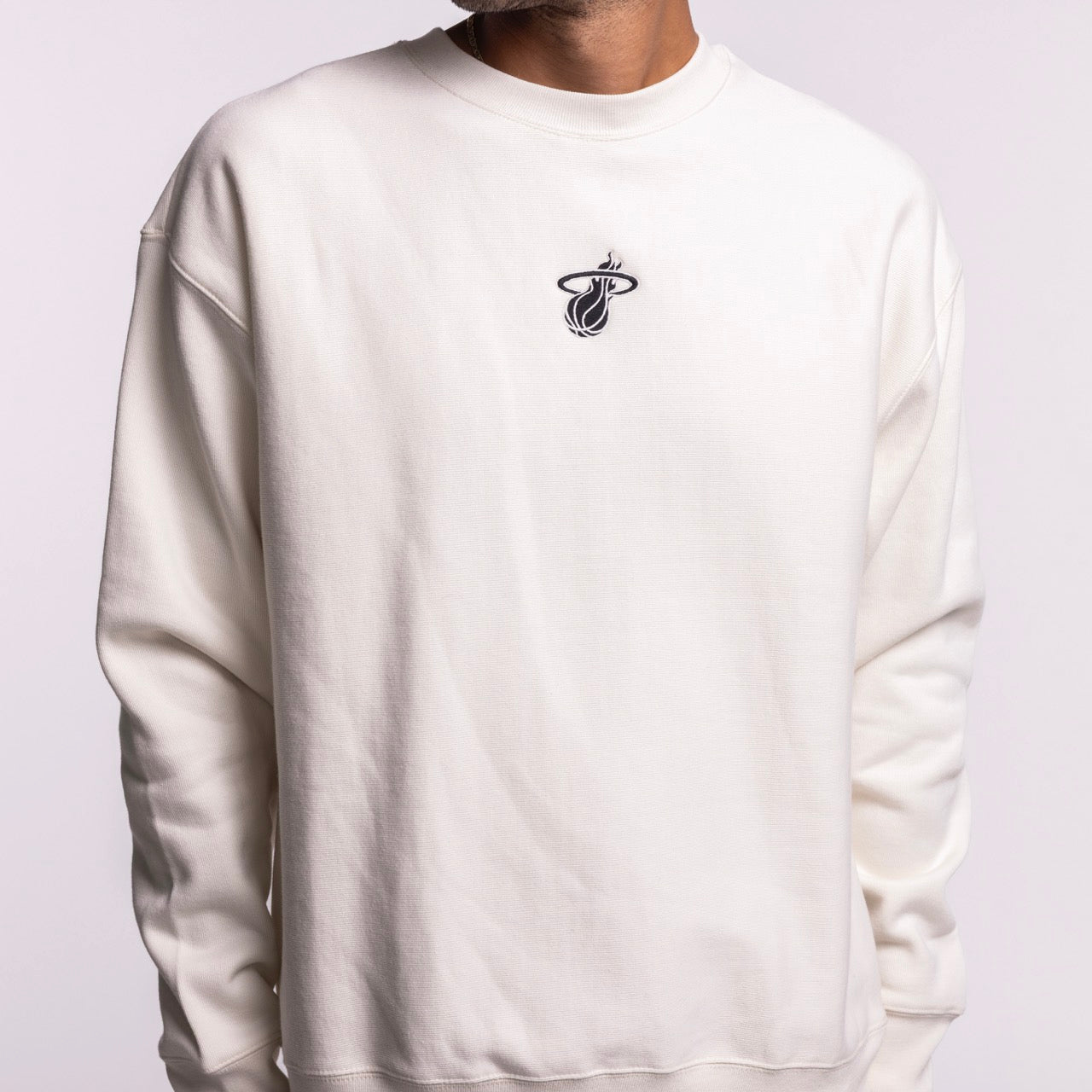 A person wears the '47 Brand Miami HEAT Cream Logo Foundation Crewneck, featuring the team logo on the chest. The cotton-polyester sweatshirt has a soft brushed interior for all-day comfort, shown against a light background.