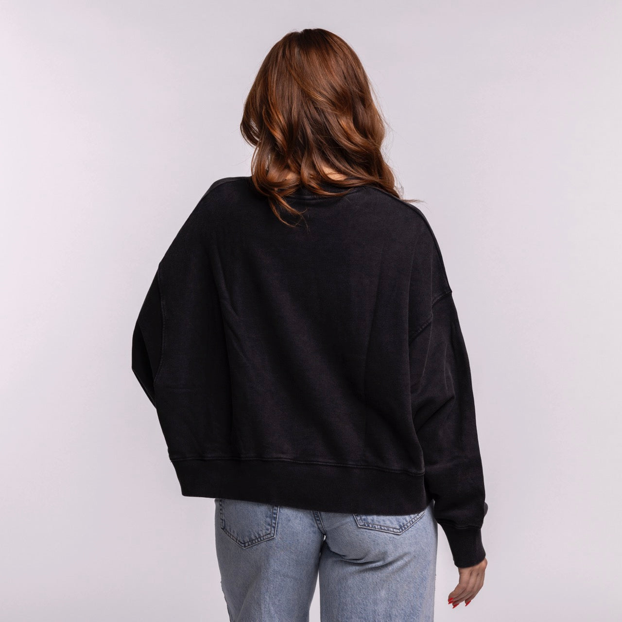 A woman with wavy brown hair wears the New Era Miami HEAT Original Vice Nights Washed Women's Crewneck, standing with her back to the camera against a plain light background.