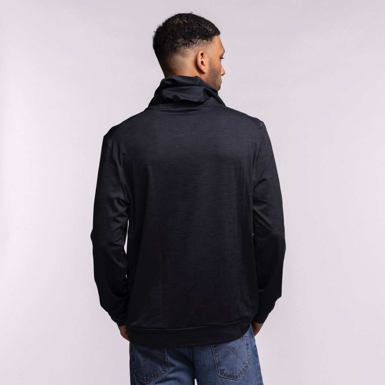 A man stands with his back to the camera, wearing a black Nike Miami HEAT Restore Pullover Hoodie and blue jeans, set against a plain light background.