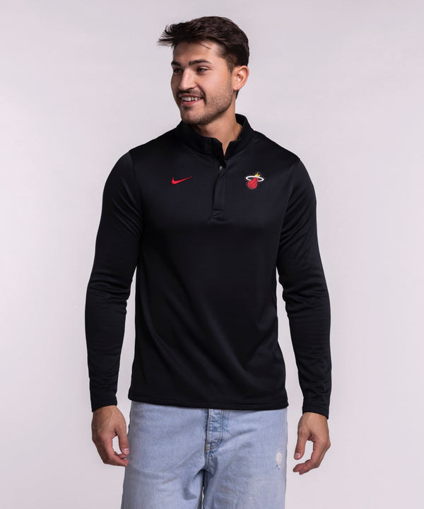 A man in light blue jeans smiles while wearing the Nike Miami HEAT Black Logo 1/4 Zip—a lightweight, sweat-wicking long-sleeve top with a red Nike logo and team emblem—standing against a plain light background.