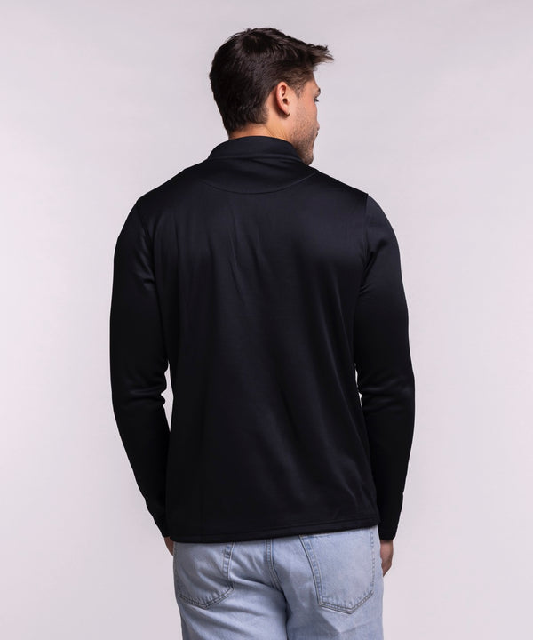 A man in light blue jeans smiles while wearing the Nike Miami HEAT Black Logo 1/4 Zip—a lightweight, sweat-wicking long-sleeve top with a red Nike logo and team emblem—standing against a plain light background.