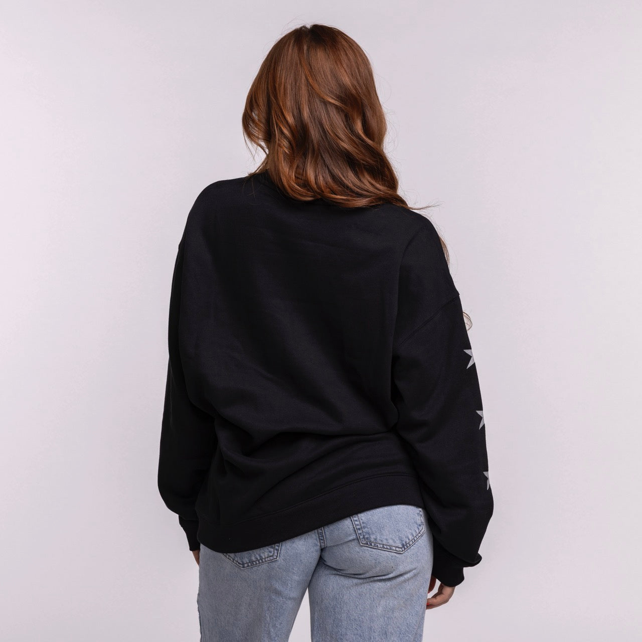 A person with long brown hair, wearing the '47 Brand Miami HEAT Original Vice Nights 1988 Women's Crewneck and light blue jeans, faces away from the camera against a plain light background. Machine wash cold.