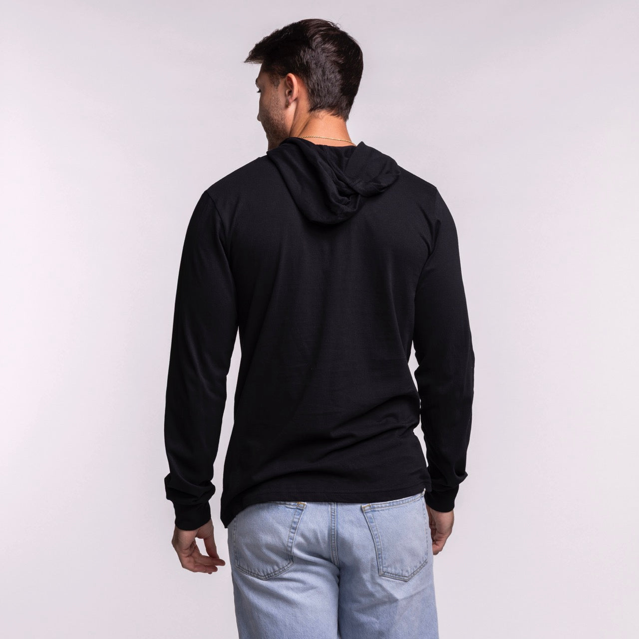 A man faces away from the camera, wearing a black Sportiqe Miami HEAT Solano Logo Hoodie and light blue jeans against a plain white background.