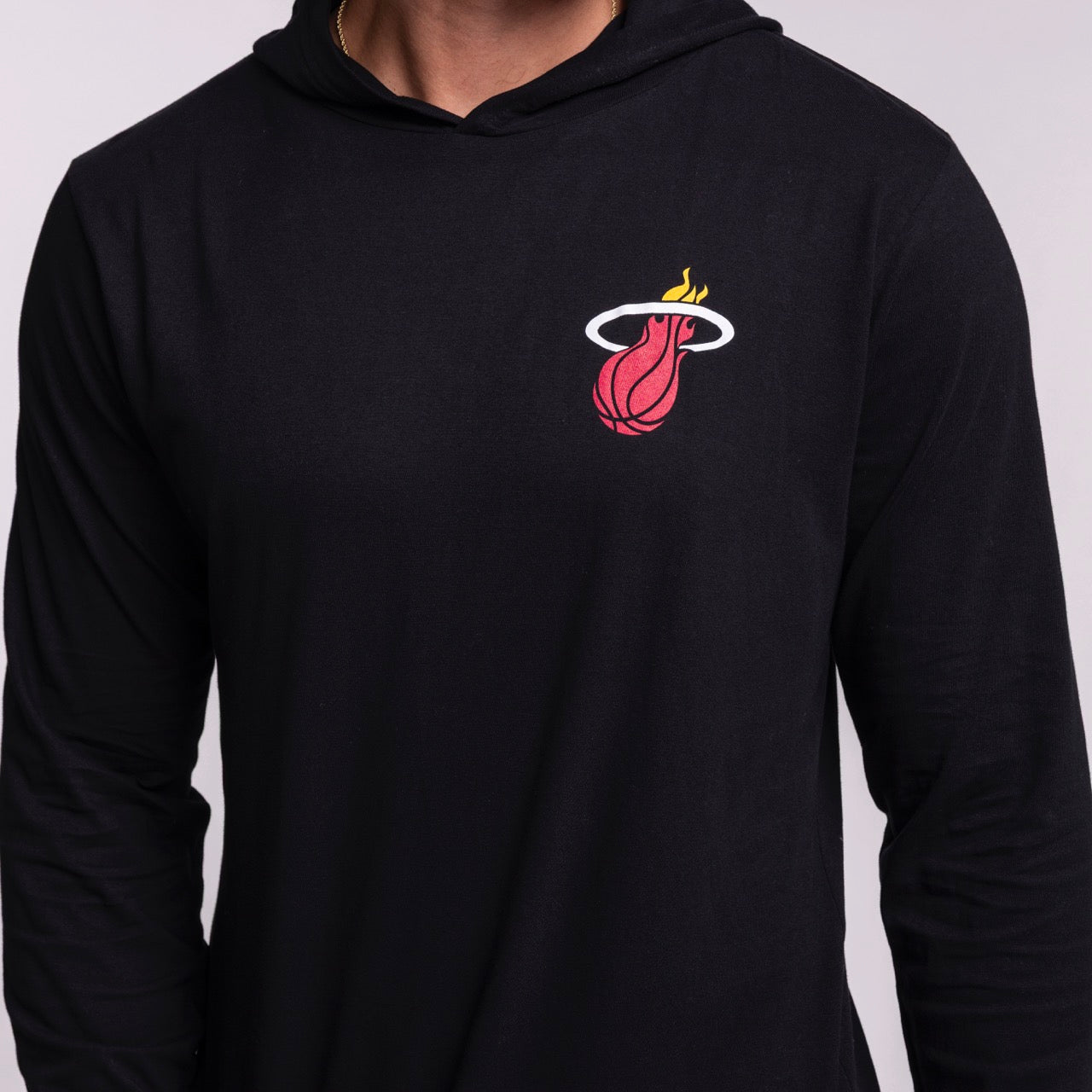 A person wearing the Sportiqe Miami HEAT Solano Logo Hoodie, a black standard fit made from 100% cotton. Features a flaming basketball logo on the left chest. Easy care—just machine wash cold. Brand: Sportiqe.