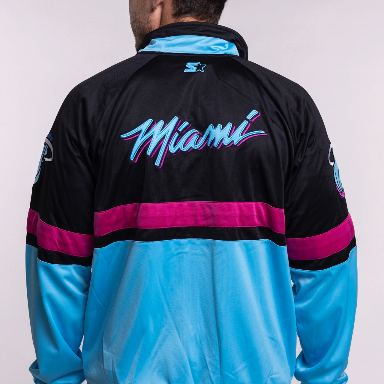 A person wearing the G-III Sports Miami HEAT Original Vice Nights Track Jacket in black, pink, and blue with stylized 