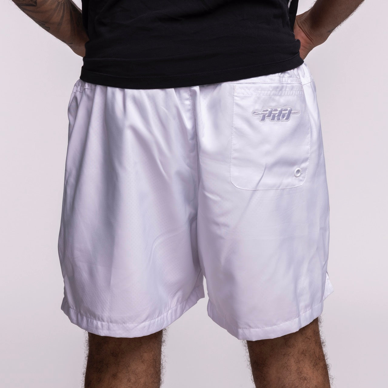 Wearing Pro Standard Miami HEAT White Out Woven Shorts in standard fit polyester with a PRO logo on the back pocket, someone stands hands on hips in a black shirt against a plain light background. Wash with like colors.