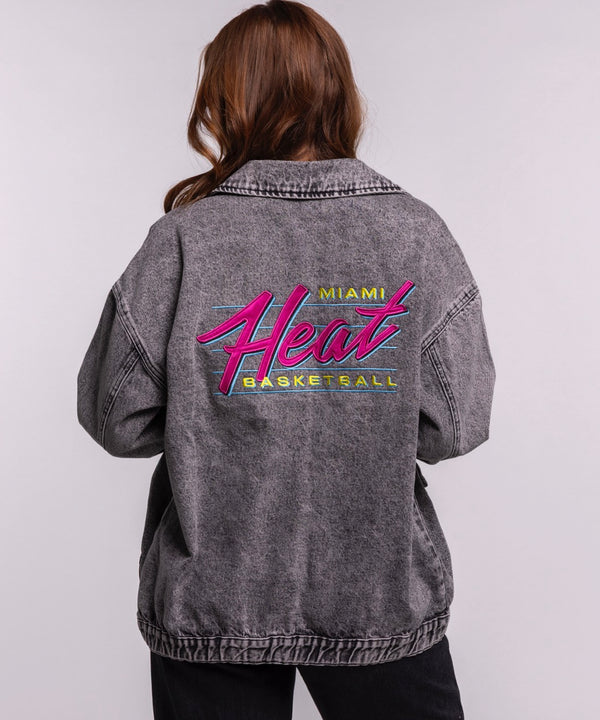 A young woman with long brown hair wears the Court Culture X The Wild Collective Original Vice Nights Denim Patch Unisex Jacket over a white shirt and black pants, standing against a plain light background.