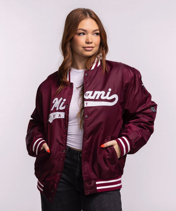 A man faces forward wearing a Hype and Vice Miami HEAT Varsity Jacket in maroon with white script, paired with a white t-shirt and black pants, set against a plain light background.