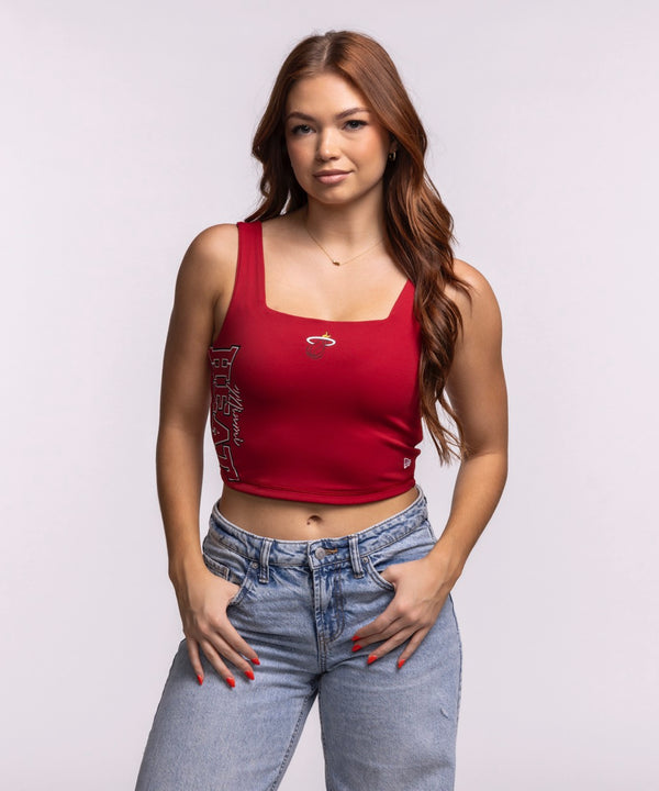 A woman with long auburn hair wears the New Era Miami HEAT Reversible Women's Tank and light blue jeans, standing with hands on hips against a plain background—a stylish way to show team pride.