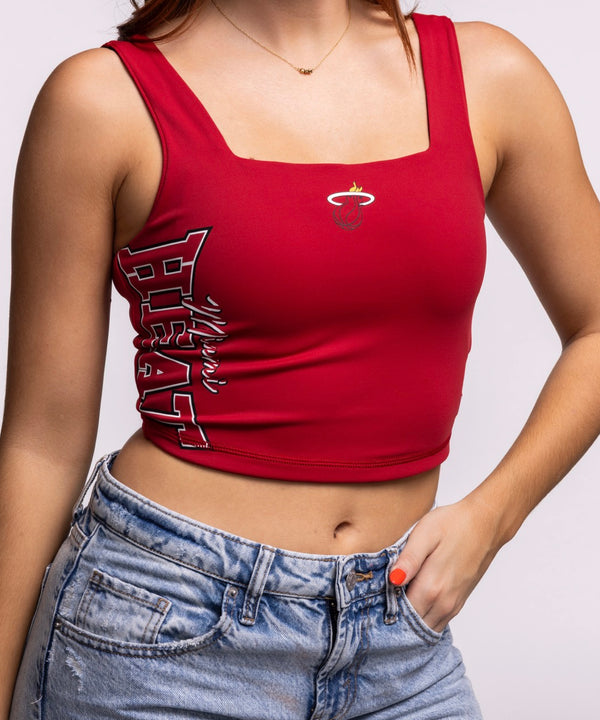A woman with long auburn hair wears the New Era Miami HEAT Reversible Women's Tank and light blue jeans, standing with hands on hips against a plain background—a stylish way to show team pride.