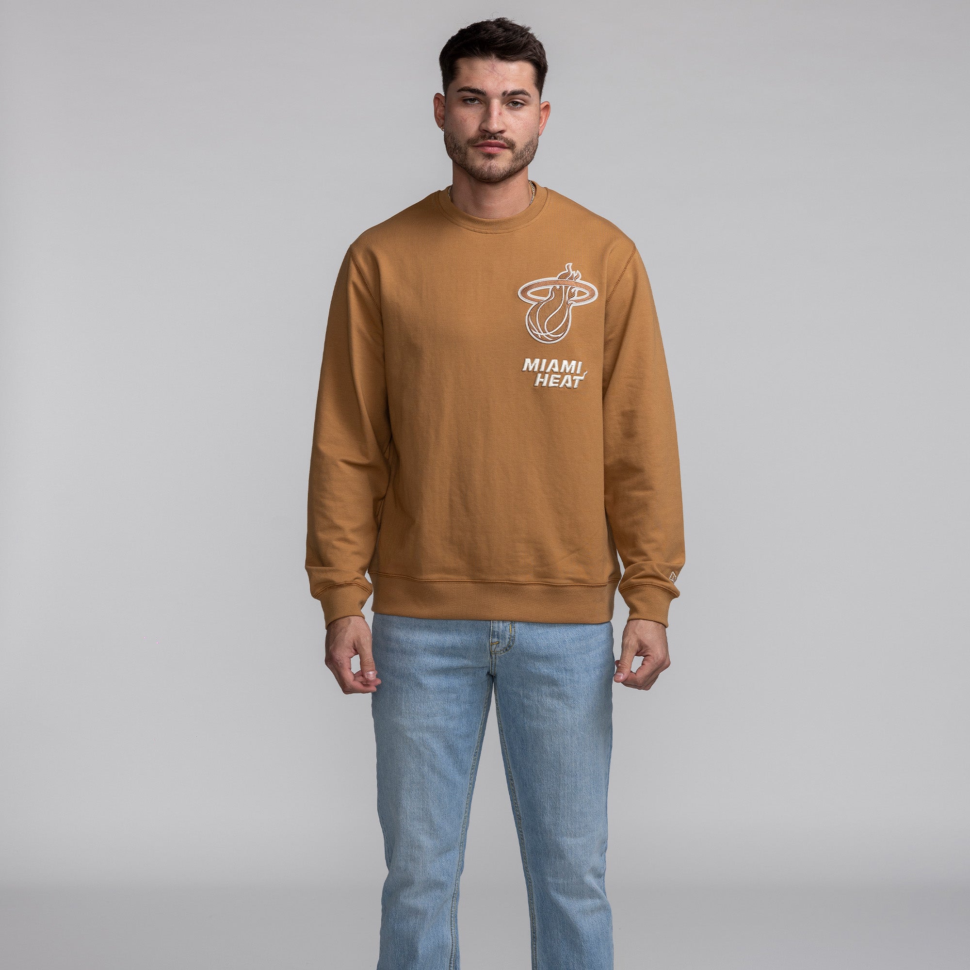 Tan New Era Miami HEAT crewneck sweatshirt with white logo, worn with light blue jeans. - New Era Miami HEAT Tan Crewneck