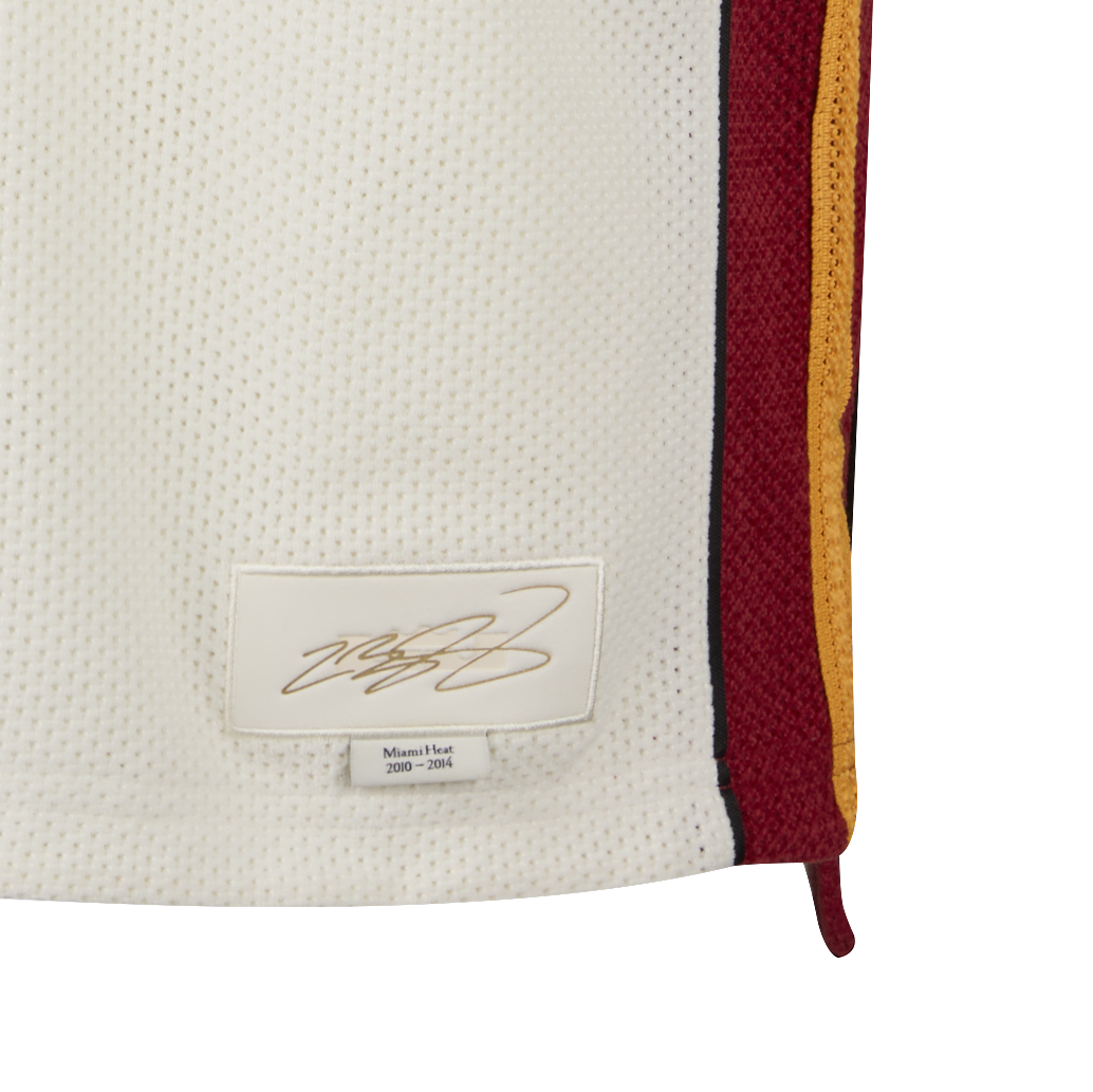 Close-up of a white Miami HEAT LeBron James Nike Forever King Jersey with red and yellow side panels, sewn autograph patch, 2010-2014 label, and Nike Dri-FIT sweat-wicking technology for comfort on and off the court.