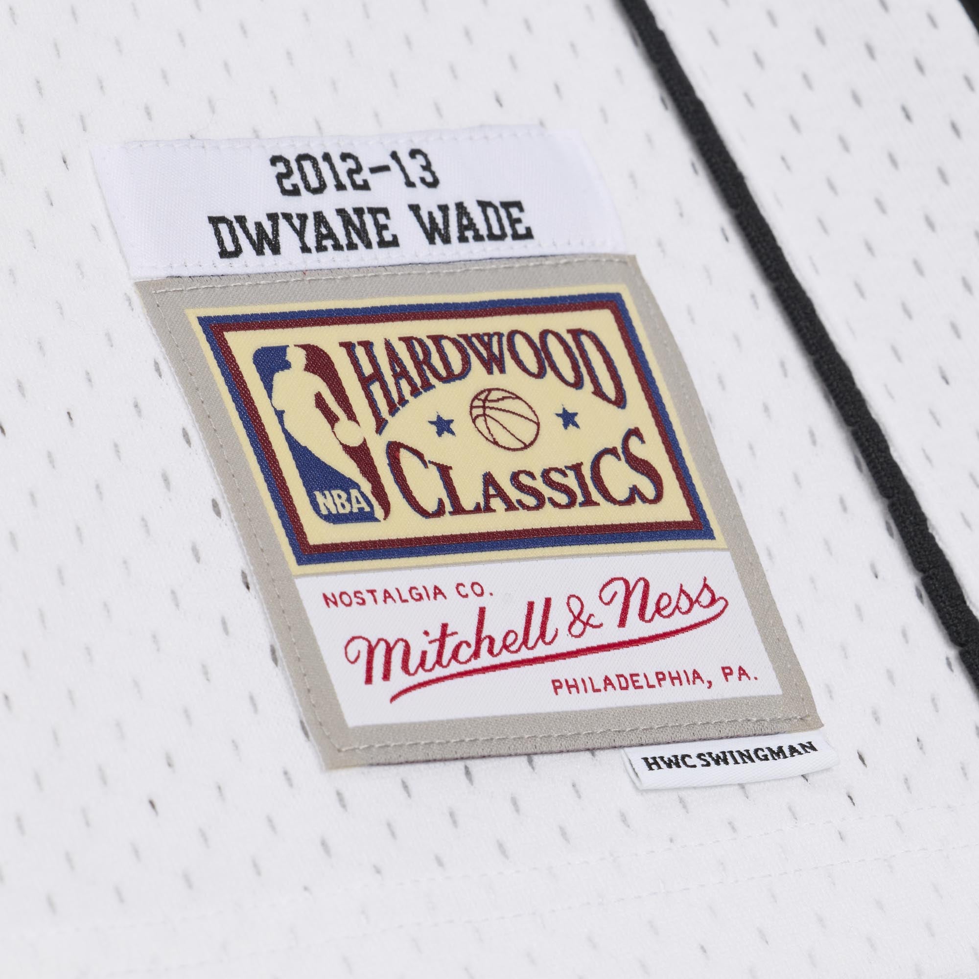 Close-up of the woven jock tag on a Dwyane Wade Mitchell & Ness Miami HEAT White Hot 2012-13 Swingman Jersey, displaying 2012-13 DWYANE WADE above an NBA Hardwood Classics patch.